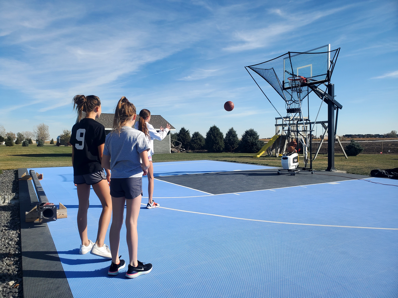 Teens practice their basketball throws on blue backyard court