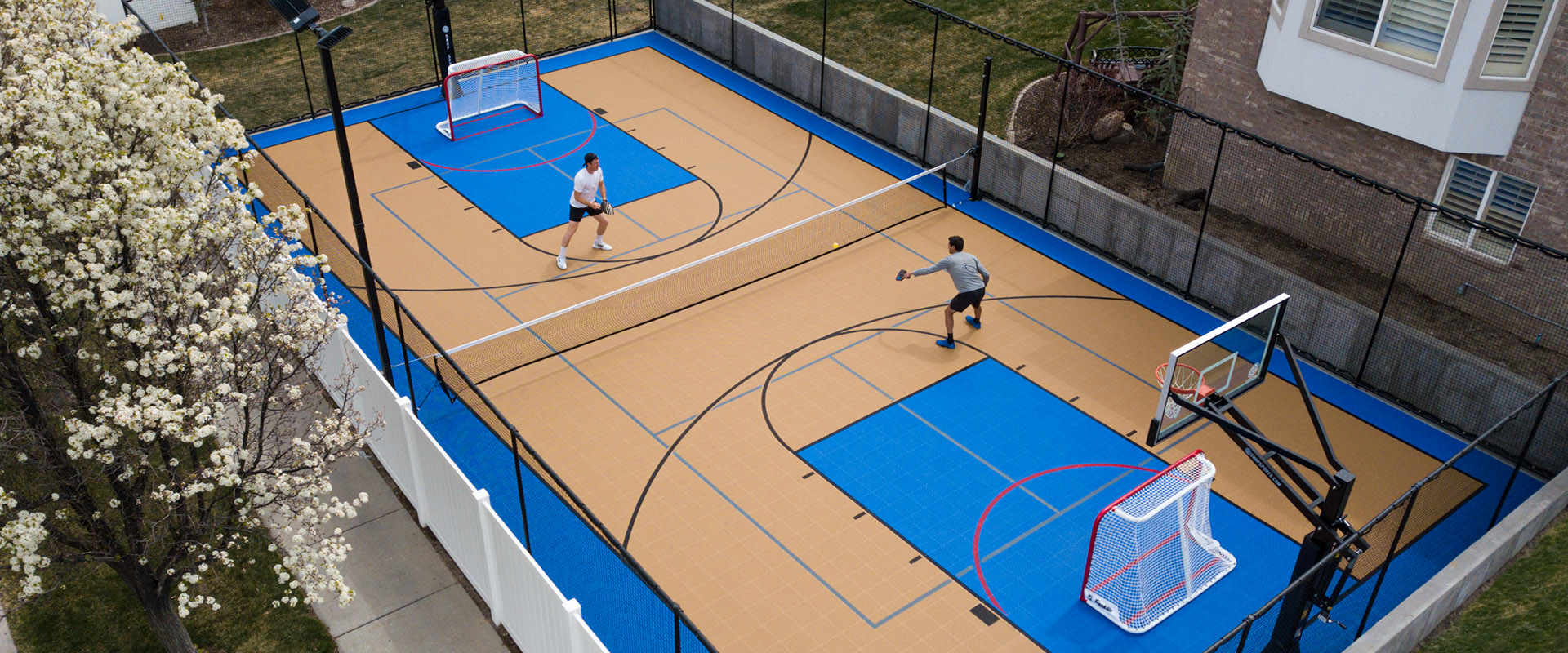 Two men playing Pickleball on a backyard. multi-court in sand and bright blue colors