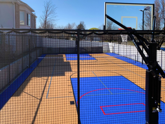 A Bright Blue and Orange backyard multi-court with hoops, nets, and fencing
