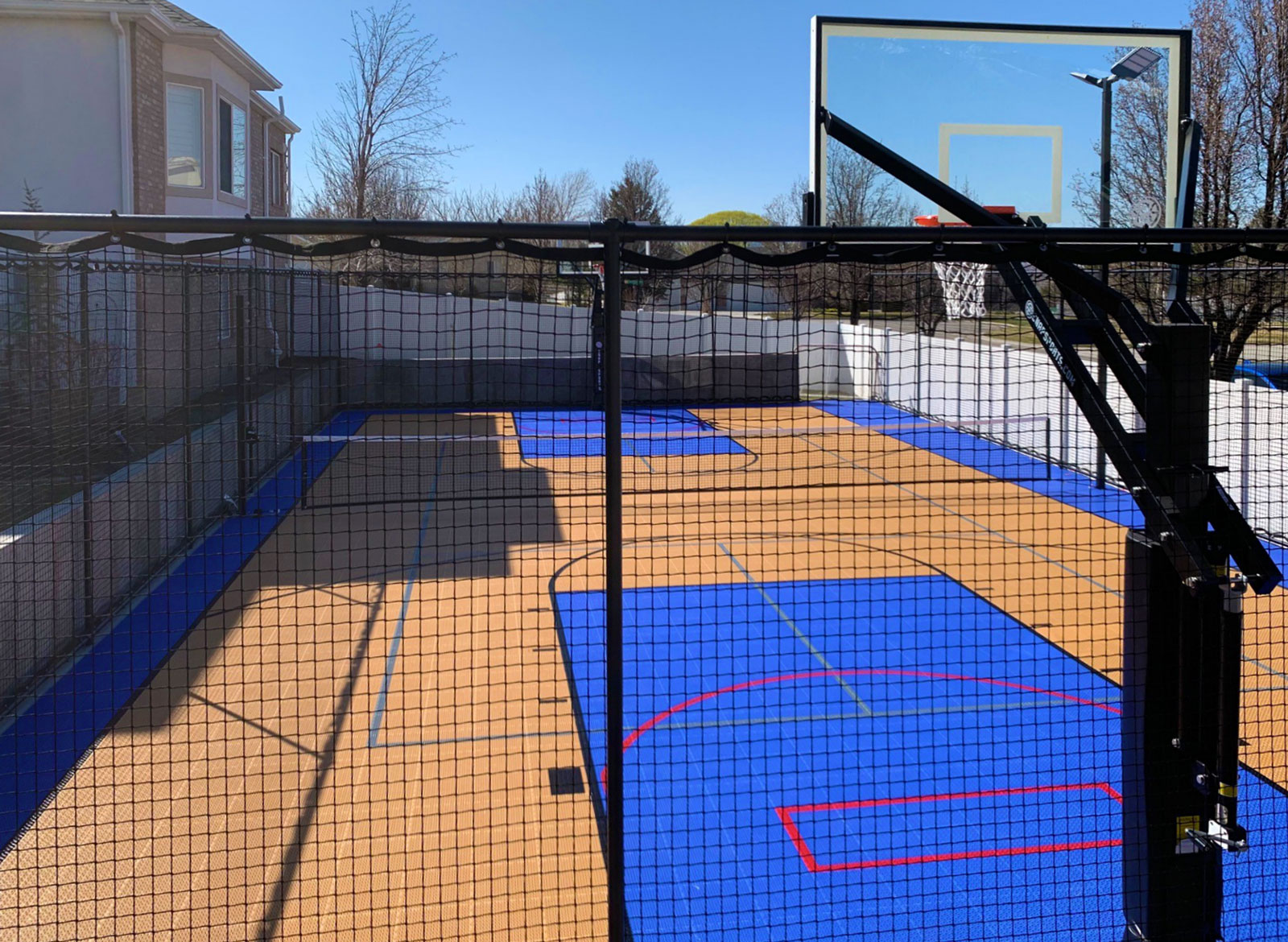 A Bright Blue and Orange backyard multi-court with hoops, nets, and fencing