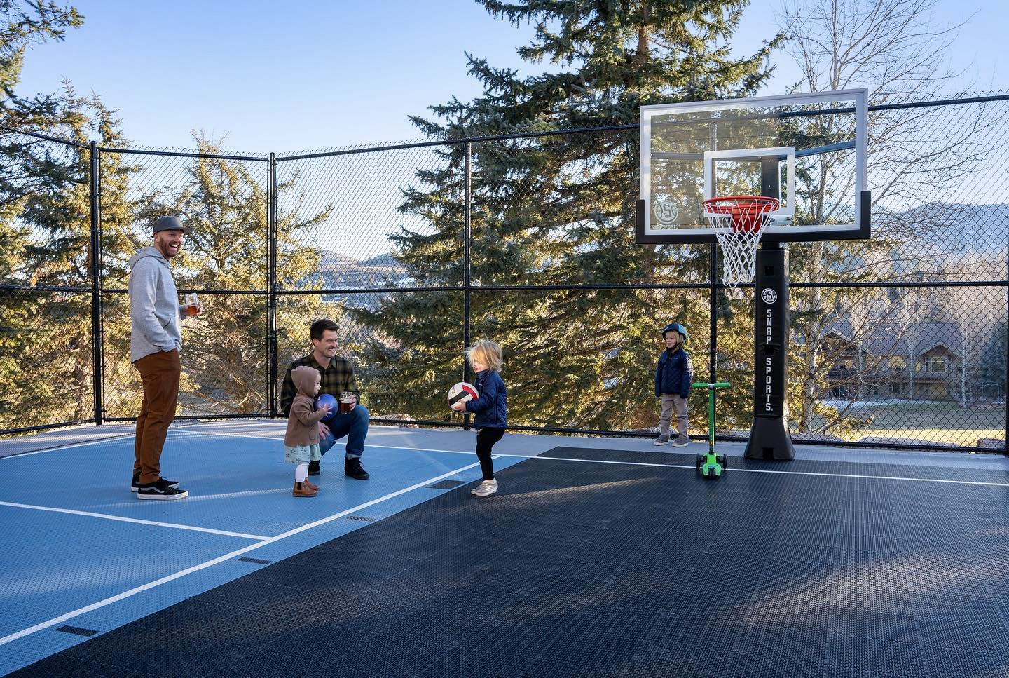 Dads and kids playing on a multi-court, with basketball hoop adjusted to kid height