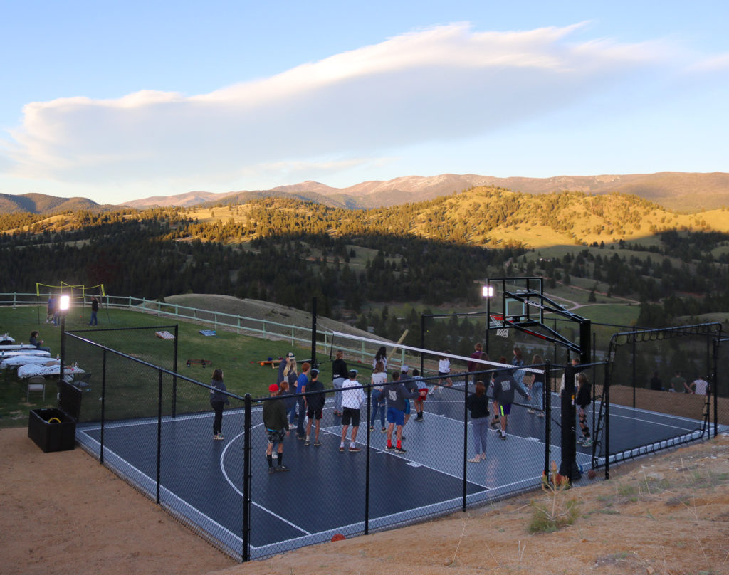 People playing on a gray and graphite backyard half-court, with lights on