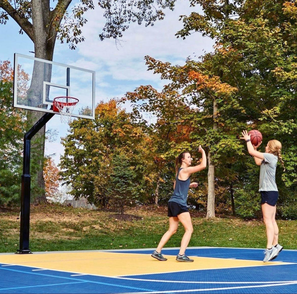Two girls playing basketball on a blue and yellow backyard court
