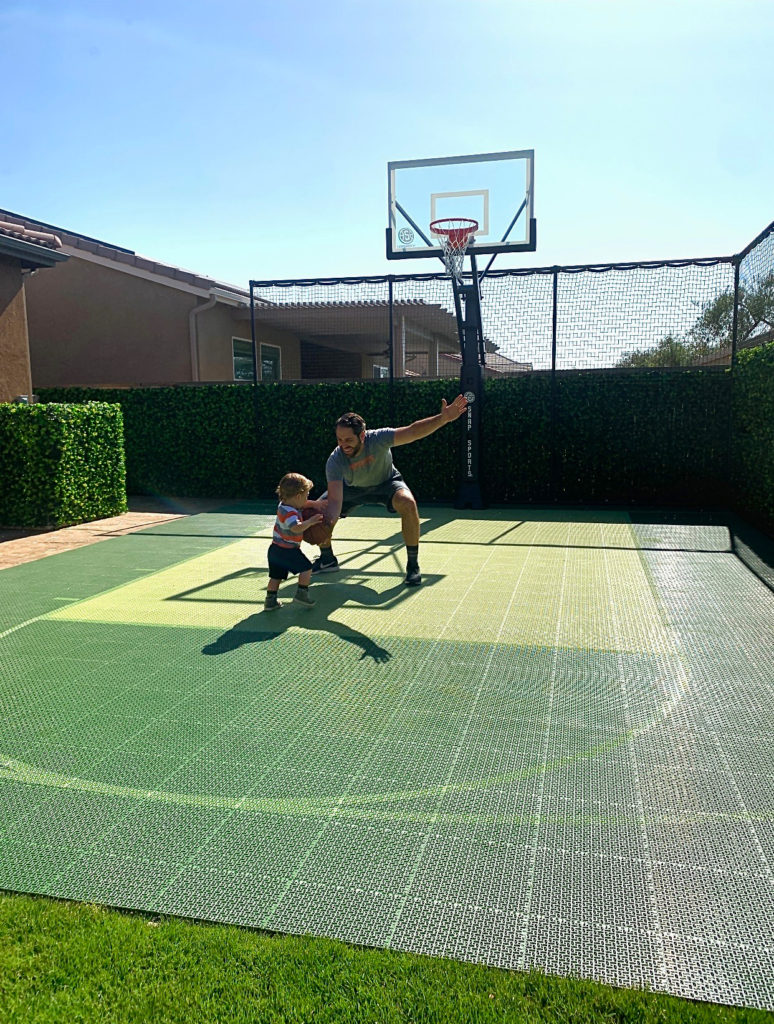 A father and his child playing on their green basketball court