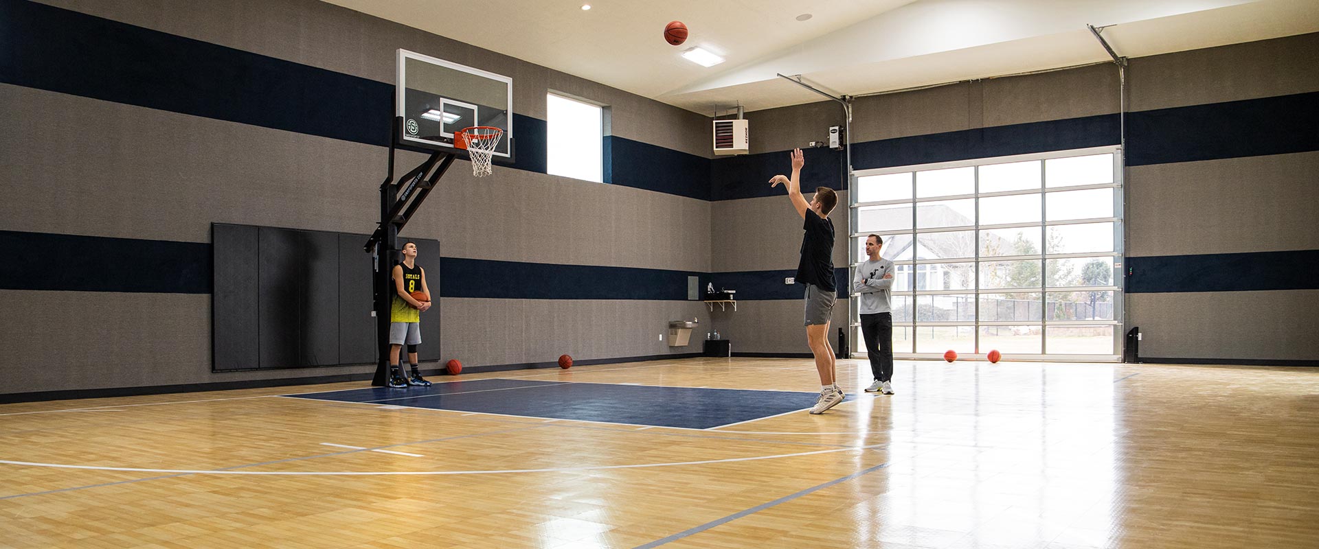 Father and sons practice drills on their indoor basketball court