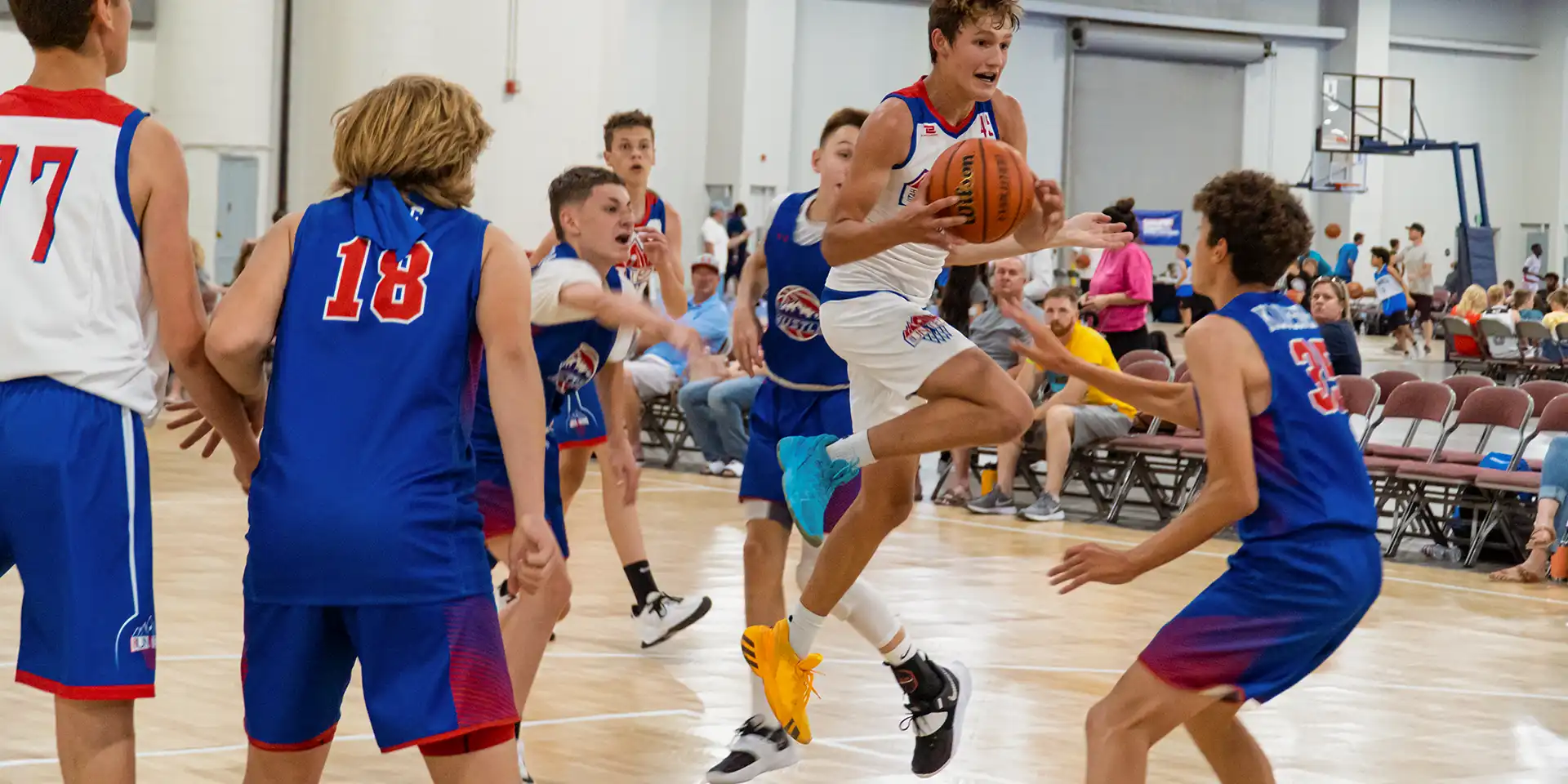 commercial sports flooring opt A young man jumps for a layup against the opposing team at an AAU basketball event.
